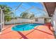 Sparkling in-ground pool inside screened enclosure with a red deck and tropical landscaping at 2217 Stacy Ct, Dunedin, FL 34698