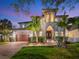 Elegant home with mature palms, beautiful landscaping, a brick driveway, and a welcoming front porch, all illuminated at twilight at 150 Chippewa Ave, Tampa, FL 33606
