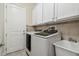 Laundry room featuring white cabinets, sink, tile backsplash, and modern washer and dryer units at 2632 Tarragona Way, Wesley Chapel, FL 33543