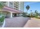 Exterior shot of the building entrance with a brick paved driveway and tropical landscaping under a blue sky at 736 Island Way # 303, Clearwater Beach, FL 33767