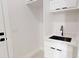 A modern laundry room featuring a stainless steel sink, white cabinets, and dark hardware at 5051 Gevalia Dr, Brooksville, FL 34604