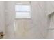 Marble tiled walk-in shower featuring a rainfall shower head, a shower niche, and a large window at 5051 Gevalia Dr, Brooksville, FL 34604