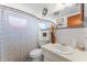 Well-lit bathroom featuring a sink vanity, toilet, patterned shower curtain, and decorative mirror at 3748 Redwood Dr, Holiday, FL 34691