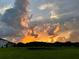 Backyard with vast green space and pond reflecting a fiery sunset, framed by trees and cloudy skies at 4114 Dovetail Ln, Palmetto, FL 34221