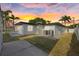 Exterior view of the home with a grassy lawn, palm trees, and a vibrant sunset backdrop at 504 Driftwood E Dr, Palm Harbor, FL 34683
