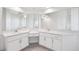 White bathroom with dual sinks, white cabinets, large mirrors and gray tile flooring at 13096 Linzia Ln, Spring Hill, FL 34609