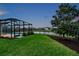 Beautiful backyard featuring a screened pool, lush green lawn, and a tranquil water view at dusk at 28683 Lucero Ln, Wesley Chapel, FL 33543