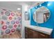 Vibrant bathroom with bright blue accent wall, large round mirror, and colorful shower curtain at 11368 93Rd St, Largo, FL 33773