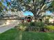 Charming home exterior featuring lush landscaping and a vibrant red front door, shaded by a mature tree at 6805 Monet Cir, Temple Terrace, FL 33617