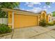 Attached two-car garage with a yellow door and mature landscaping around the driveway at 23211 Lucerne Pl, Land O Lakes, FL 34639