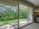 A view of the outdoor patio area through large glass sliding doors with verdant landscaping at 1353 Curlew Rd, Dunedin, FL 34698