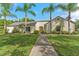 Charming single-story home with a well-manicured lawn and mature palm trees lining the walkway to the front door at 1591 Chestnut W Ct, Palm Harbor, FL 34683