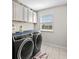 Well-lit laundry room with overhead cabinets, tile flooring, and modern washer and dryer at 7513 S Sherrill St, Tampa, FL 33616