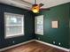 Bedroom with dark green walls, hardwood floors, ceiling fan and two windows at 832 King Leon Way, Sun City Center, FL 33573