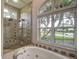Bright walk-in shower and soaking tub with large windows overlooking manicured yard at 5460 Millbrook Way, Palm Harbor, FL 34685
