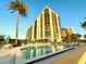 Exterior view of tall condo building by pool and palm trees against a clear blue sky at 690 Island Way # 707, Clearwater Beach, FL 33767
