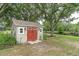 This backyard shed includes red doors and is shaded by mature trees near a pond at 12304 Freesia Ct, Riverview, FL 33569