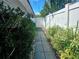 Side yard with a gray paver walkway leading to a gate, bordered by green shrubbery and a white fence at 1345 S Evergreen Ave, Clearwater, FL 33756
