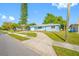 Single-story light blue home featuring a well-maintained lawn and mature trees on a sunny day at 1431 Kings Hwy, Clearwater, FL 33755