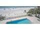 Aerial view of a pool adjacent to a white sand beach with palm trees and clear blue water at 19700 Gulf Blvd # 403, Indian Shores, FL 33785