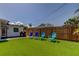 Well-kept backyard featuring artificial turf, a white house, grilling area and a wooden fence at 2488 Del Rio Way, Dunedin, FL 34698