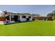 A spacious backyard with artificial turf, a white house, an area for grilling, and a privacy fence at 2488 Del Rio Way, Dunedin, FL 34698