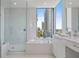 Bright bathroom featuring a glass-enclosed shower, soaking tub, and large window with a cityscape view at 100 1St N Ave # 1005, St Petersburg, FL 33701