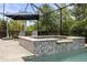 A screened hot tub is adjacent to the pool and is surrounded by travertine tile and lush landscaping at 19810 Prince Benjamin Dr, Lutz, FL 33549