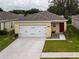 View of a single-story home with a two-car garage, red front door, neat landscaping, and a driveway at 3686 Zephyr Preserve Pl, Zephyrhills, FL 33541