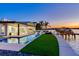 Elegant home featuring a pool, manicured lawn, and dock with a boat, all set against a picturesque waterfront backdrop at dusk at 16496 Redington Dr, Redington Beach, FL 33708