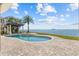 Stunning pool with stone patio, palm trees, and waterfront views create a luxurious outdoor oasis at 2402 Baywood W Dr, Dunedin, FL 34698