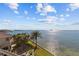 Elegant home with waterfront access, featuring a covered outdoor lounge and lush palm trees along the shoreline at 2402 Baywood W Dr, Dunedin, FL 34698