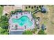 Aerial view of a turquoise community pool, complete with lounge chairs, palm trees, and surrounding amenities at 14434 Scottburgh Glen Dr, Wimauma, FL 33598