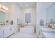 Bathroom with a luxurious soaking tub between two vanities, each featuring white cabinets and gold hardware at 111 Alafia Estates Ln, Plant City, FL 33567