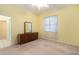 Bedroom featuring a dresser with mirror, window with white curtains, light yellow walls, and neutral carpet at 3545 E Lake Dr, Land O Lakes, FL 34639