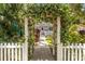 View of the purple home with white trim and fence through a flower covered archway at 522 James St, Dunedin, FL 34698