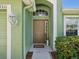 The charming front door with a welcome mat is surrounded by green plants and exterior lighting at 1211 Penny Ct, Dunedin, FL 34698