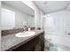 Bright bathroom with granite countertop vanity, framed mirror, and glass-enclosed shower-tub combination at 9433 Channing Hill Dr, Sun City Center, FL 33573