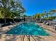 Community pool with lounge chairs, tables, and a pergola surrounded by green landscaping and palm trees on a sunny day at 1103 Coral Ln, Dunedin, FL 34698