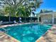 Community pool with lounge chairs, tables, a pool house and an umbrella surrounded by green landscaping at 1103 Coral Ln, Dunedin, FL 34698