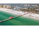 Aerial view of a lively beach with a long pier, clear water, and numerous people enjoying the sunny day at 311 Island Way # 101, Clearwater Beach, FL 33767