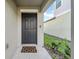 Stylish gray front door with decorative welcome mat, surrounded by neutral-toned walls and landscaping at 22196 Calisto Way, Land O Lakes, FL 34637