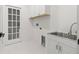 Clean, bright laundry room with shaker cabinets, stainless steel sink, and white hexagonal tiled floors at 3505 N Dartmouth Ave, Tampa, FL 33603