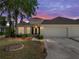 Beautiful home with a well-manicured lawn, a two-car garage, mature trees, and a lovely front garden at sunset at 10324 Chatuge Dr, San Antonio, FL 33576