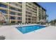 Exterior view of a condo building, pool, and tiki bar, with lounge chairs and palm trees at 650 Island Way # 204, Clearwater Beach, FL 33767