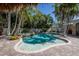A beautifully designed pool area with a hot tub, surrounded by lush palm trees and elegant brickwork at 102 Crestwood Ln, Largo, FL 33770