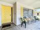 Inviting front porch with a bright yellow door, multiple chairs, and white brick exterior at 10819 Los Santos Dr, Port Richey, FL 34668