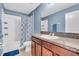 Well-lit bathroom with a single sink, wood cabinets, shower with blue curtain, and tile flooring at 14812 Boulder Pass Pl, Wimauma, FL 33598