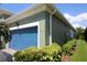 The side exterior of the home features a blue garage door and beautifully landscaped surroundings at 6417 Blue Sail Ln, Apollo Beach, FL 33572