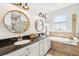 Modern bathroom featuring dual sinks, granite countertops, round mirrors, and a separate soaking tub with tile surround at 7207 Forest Mere Dr, Riverview, FL 33578